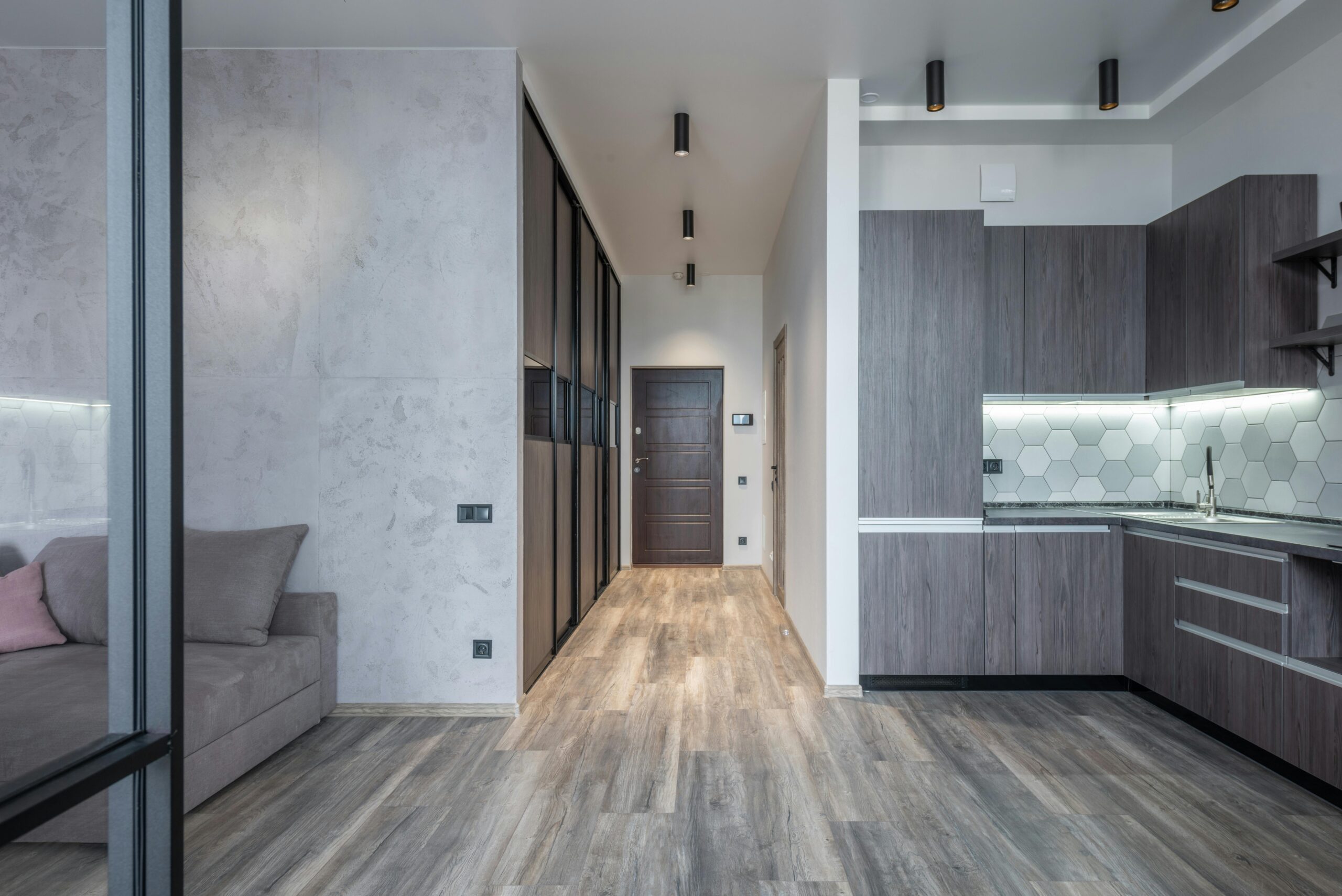 Narrow passage and contemporary kitchen interior with cabinets and cupboards against sofa at home